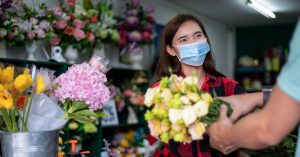 Asian Woman wearing face mask or protective mask against coronavirus crisis, Florist owner of a small florist business holding flowers for delivery to customers at her store